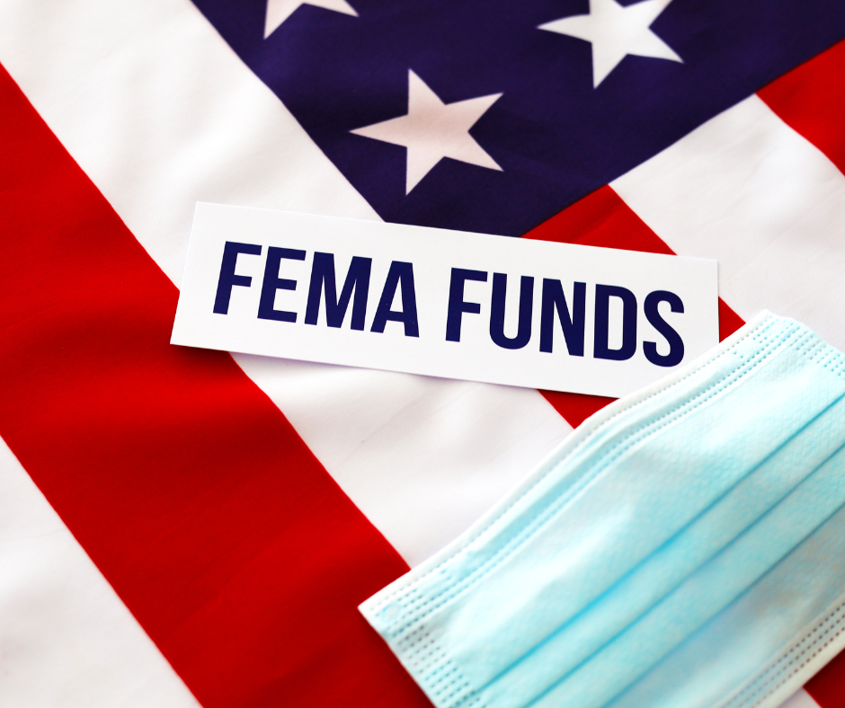 A sign with the words FEMA FUNDS laying on top of an American Flag with a health face mask laying near it.